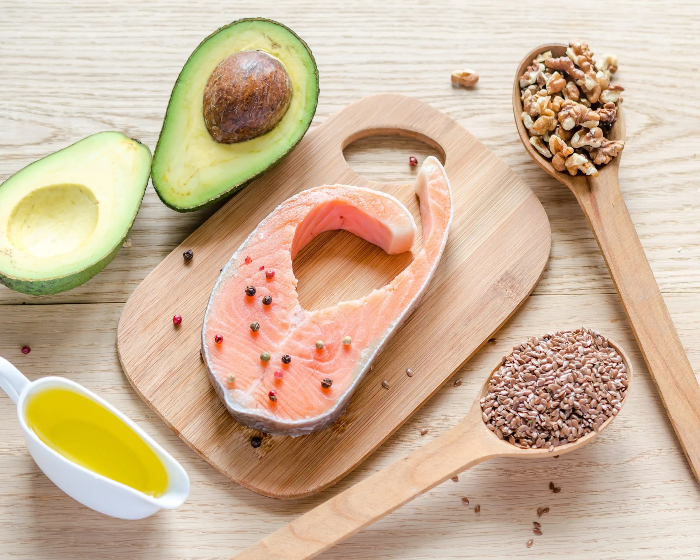 Zalm, avocado, walnoten, lijnzaad en olijfolie op een houten plank — bronnen van gezonde vetten
